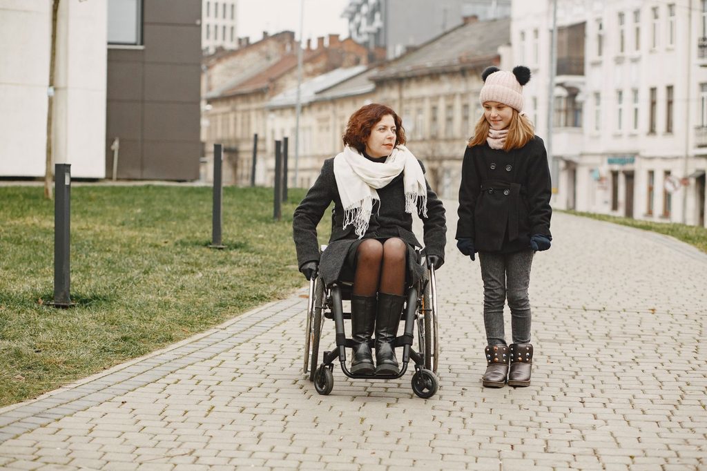 Žena na vozíku a dievča na hladkej dláždenej ulici v meste