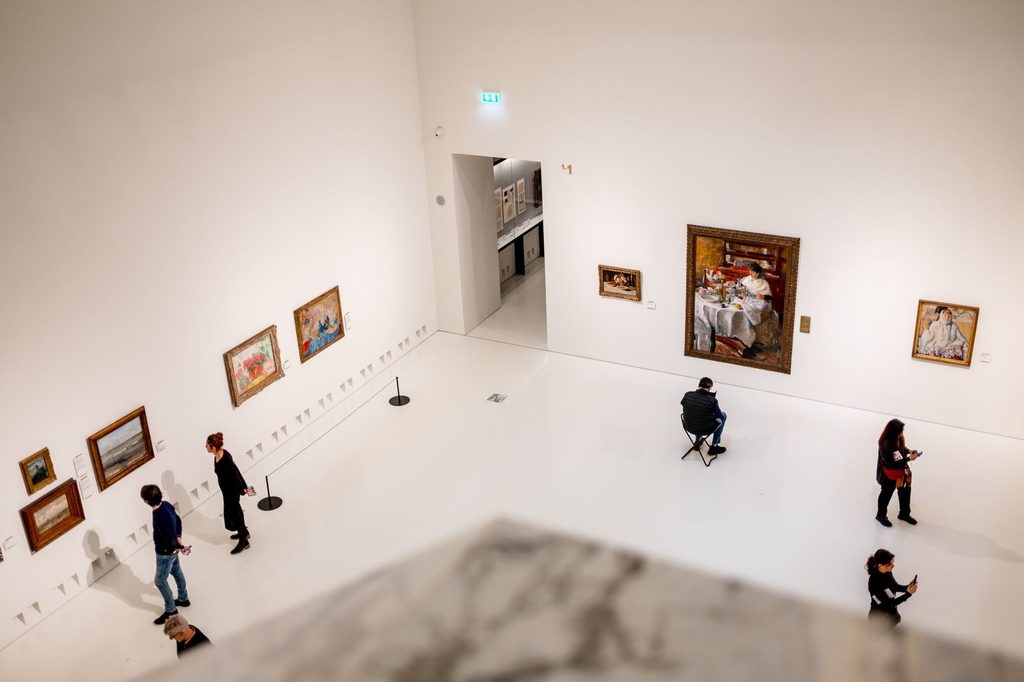 Návštevníci v galérii pozerajú na obrazy na bielych stenách